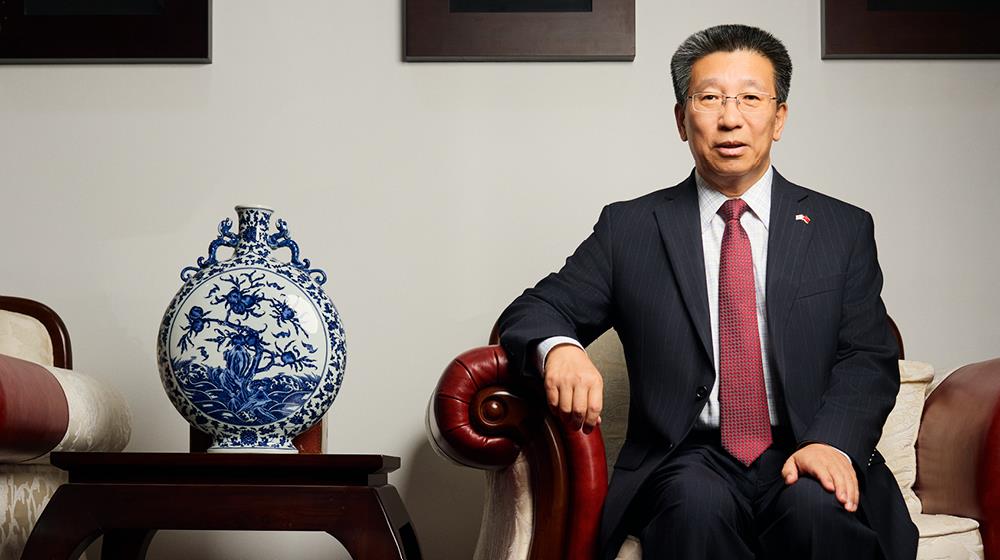 China’s Ambassador to Cyprus, Liu Yantao, sitting in an armchair next to a traditional Chinese blue & white porcelain "moon flask" vase.